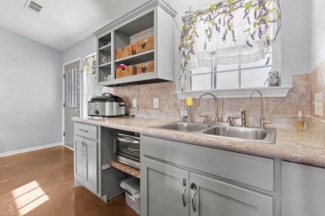 kitchen with light stone countertops, sink, gray cabinetry, and decorative backsplash