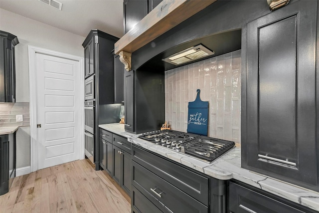 kitchen featuring light wood-style flooring, light stone counters, and dark cabinets