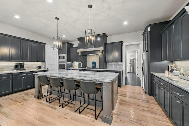 kitchen with decorative light fixtures, stainless steel appliances, a breakfast bar, light wood-style floors, and a large island with sink