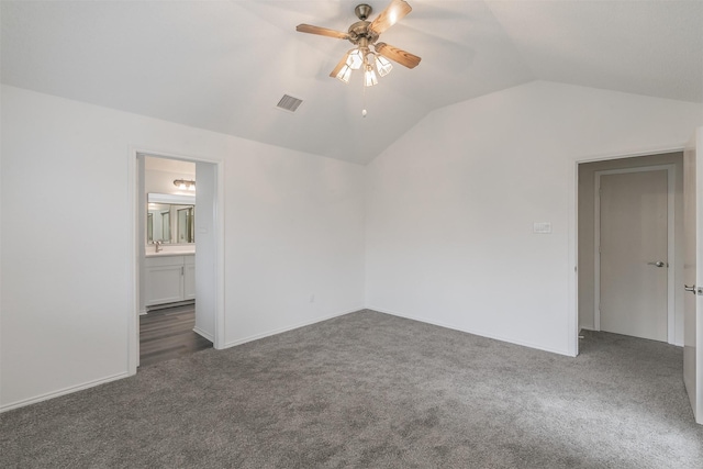 unfurnished bedroom featuring ceiling fan, ensuite bathroom, vaulted ceiling, and dark colored carpet