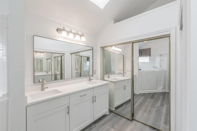 bathroom with hardwood / wood-style flooring, vanity, lofted ceiling with skylight, and a washtub