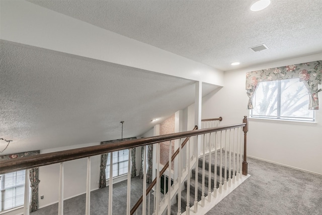 hall with lofted ceiling, carpet floors, and a textured ceiling