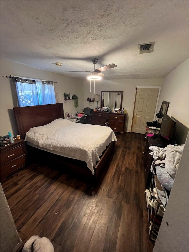 bedroom featuring a ceiling fan, visible vents, dark wood-style flooring, and a textured ceiling