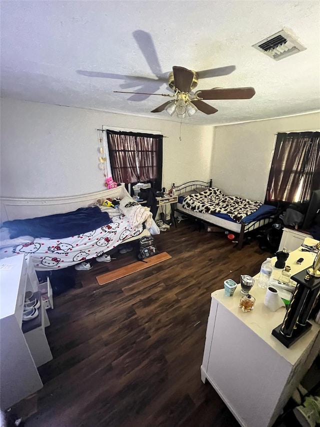 bedroom with a ceiling fan, wood finished floors, visible vents, and a textured ceiling