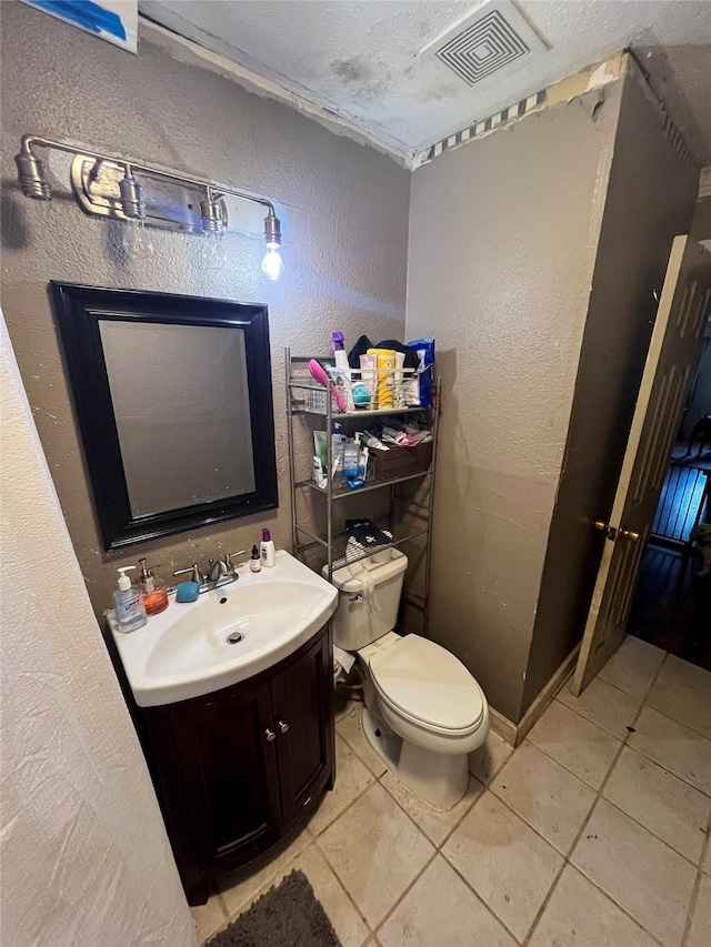 bathroom featuring vanity, visible vents, tile patterned floors, toilet, and a textured wall