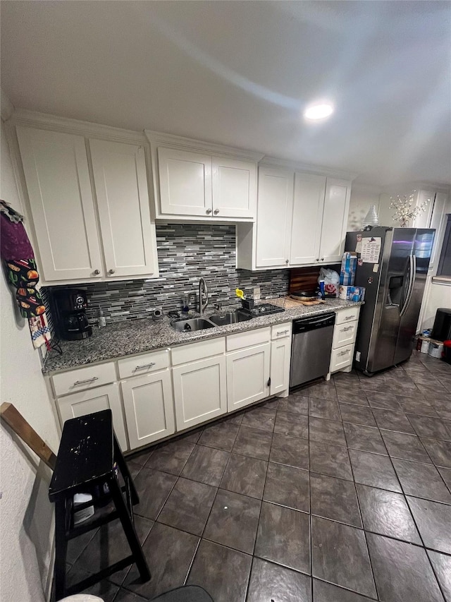 kitchen featuring tasteful backsplash, light stone counters, white cabinets, stainless steel appliances, and a sink