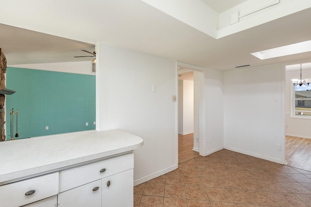 kitchen with white cabinetry, ceiling fan with notable chandelier, a skylight, and light tile patterned flooring