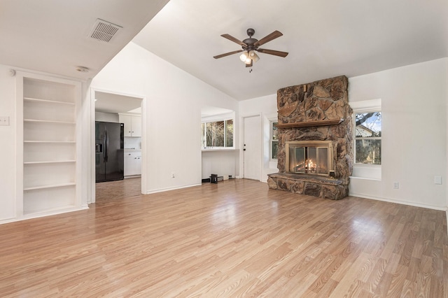 unfurnished living room featuring a stone fireplace, a healthy amount of sunlight, ceiling fan, and light wood-type flooring