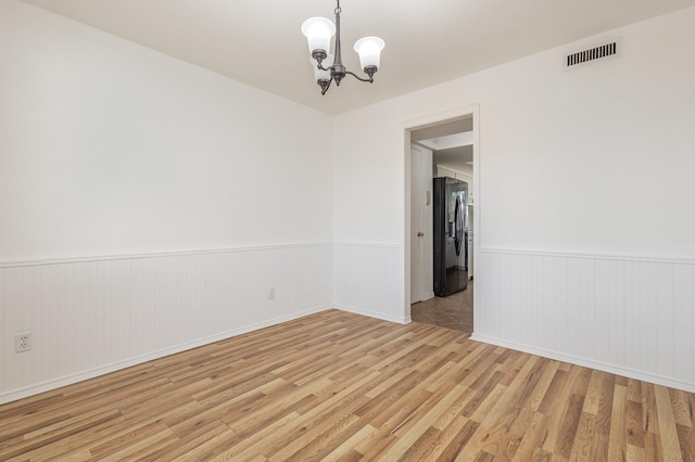 spare room featuring a notable chandelier and light wood-type flooring