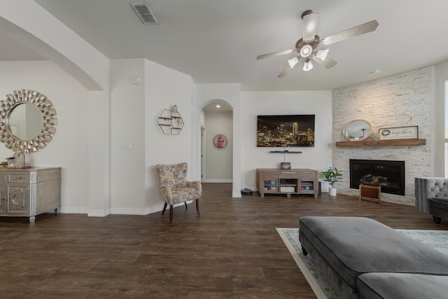 living room with a stone fireplace, dark hardwood / wood-style floors, and ceiling fan