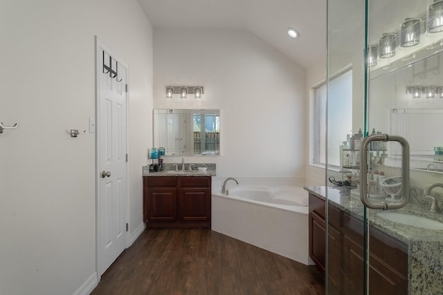 bathroom with a washtub, hardwood / wood-style floors, vanity, a wealth of natural light, and vaulted ceiling