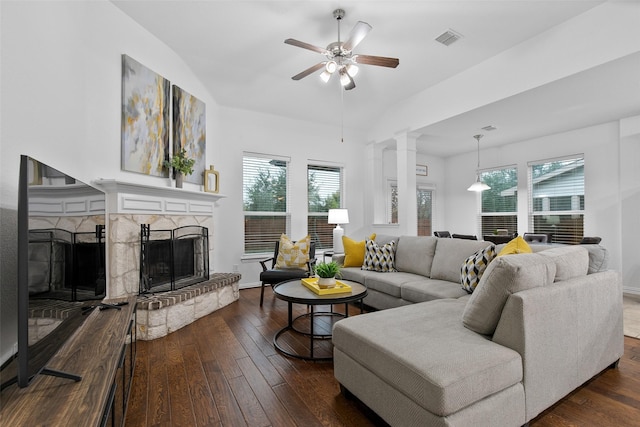 living room with a stone fireplace, dark wood-type flooring, ceiling fan, and vaulted ceiling