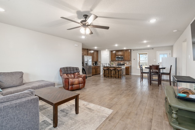 living room featuring a ceiling fan, recessed lighting, light wood-style flooring, and baseboards