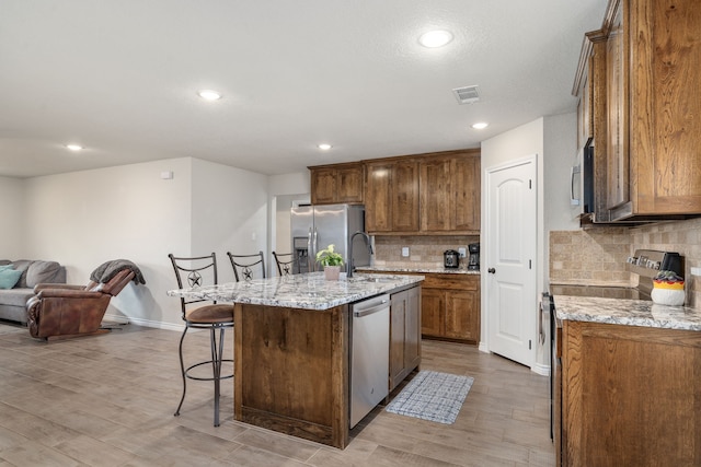 kitchen featuring appliances with stainless steel finishes, an island with sink, sink, a kitchen bar, and light stone counters