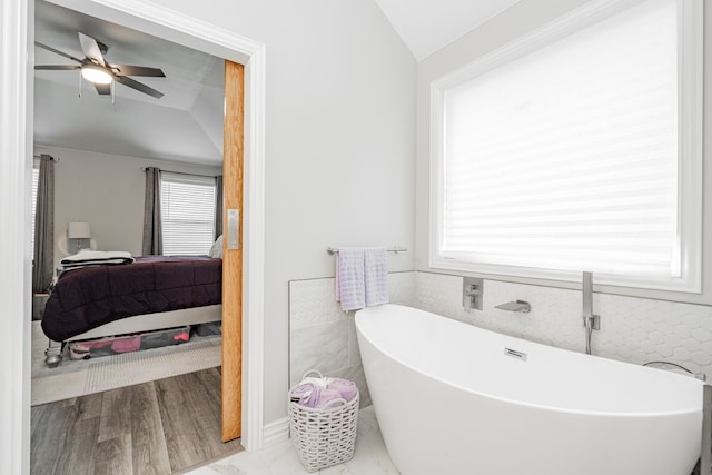 bathroom featuring ceiling fan, lofted ceiling, a bathtub, and tile walls