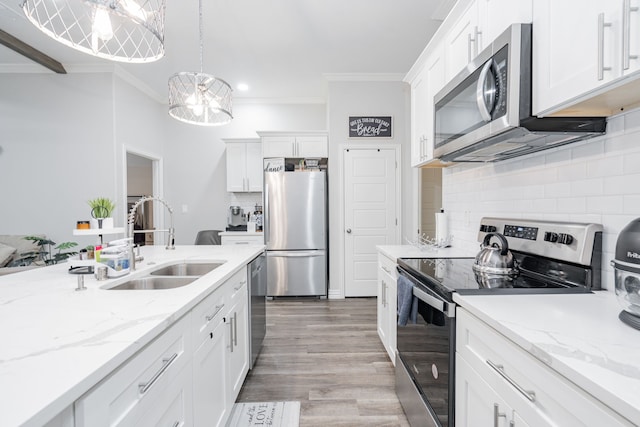 kitchen with appliances with stainless steel finishes, sink, white cabinets, hanging light fixtures, and ornamental molding