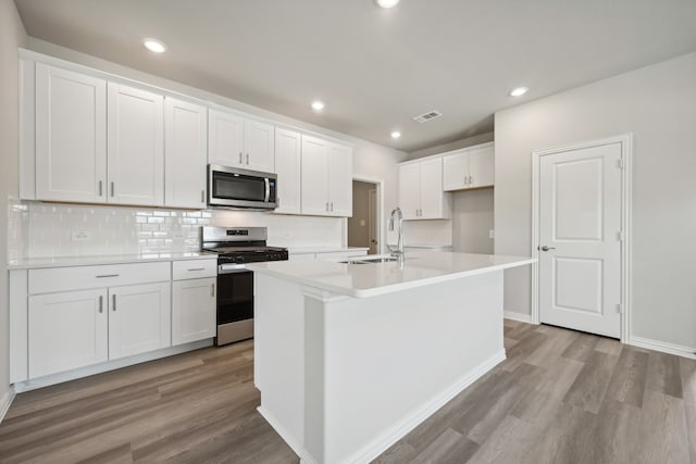 kitchen with sink, stainless steel appliances, an island with sink, white cabinets, and light wood-type flooring