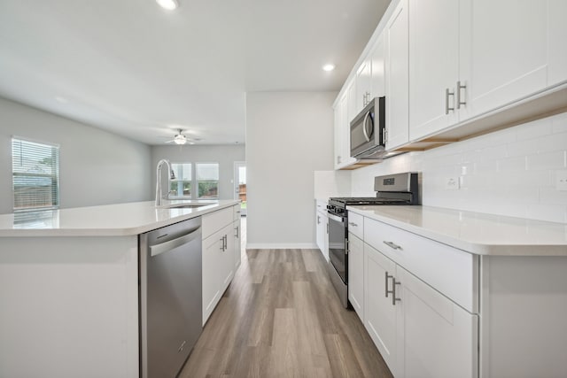 kitchen with sink, tasteful backsplash, appliances with stainless steel finishes, an island with sink, and white cabinets