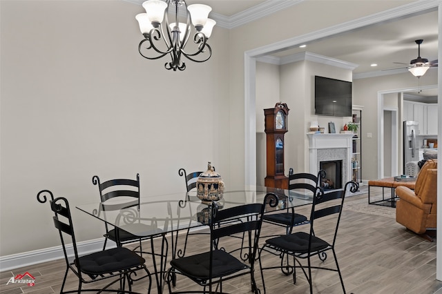 dining space with a tiled fireplace, wood-type flooring, ceiling fan with notable chandelier, and crown molding