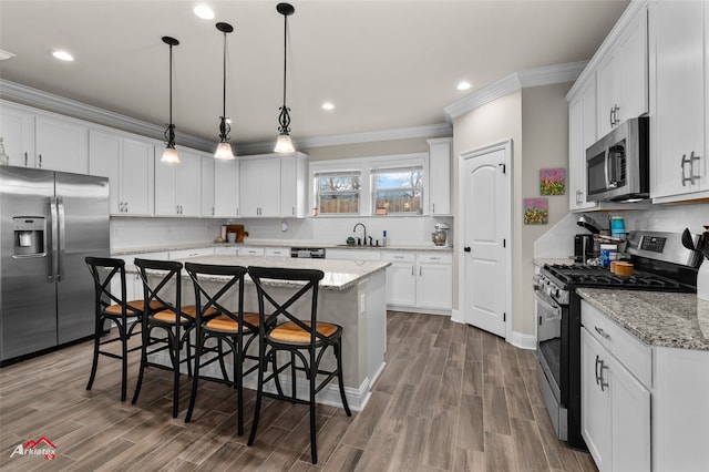 kitchen with a kitchen bar, hanging light fixtures, a kitchen island, stainless steel appliances, and white cabinets