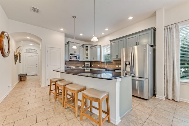 kitchen featuring a kitchen island, decorative light fixtures, gray cabinetry, dark stone counters, and stainless steel appliances