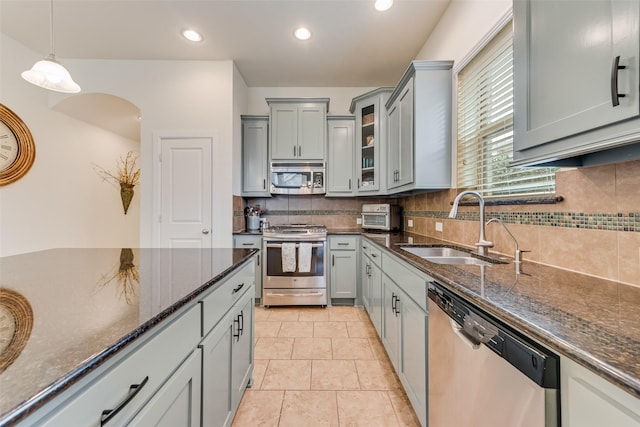 kitchen featuring sink, dark stone counters, pendant lighting, stainless steel appliances, and decorative backsplash