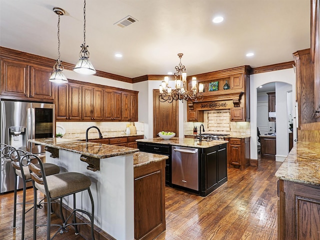 kitchen with visible vents, dark wood finished floors, a center island with sink, appliances with stainless steel finishes, and arched walkways