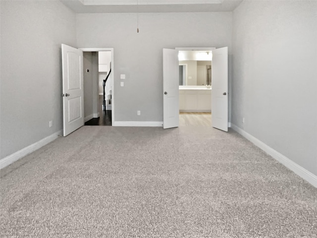 unfurnished bedroom featuring carpet flooring, ensuite bath, and a high ceiling