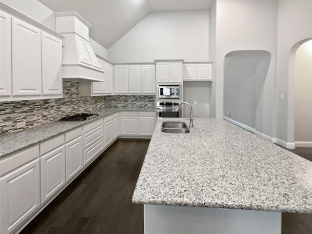 kitchen featuring appliances with stainless steel finishes, white cabinetry, sink, light stone countertops, and a center island with sink