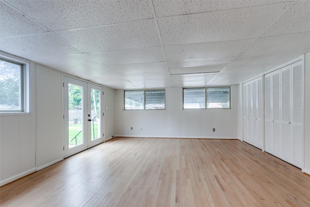 spare room featuring a paneled ceiling, light hardwood / wood-style floors, french doors, and a healthy amount of sunlight