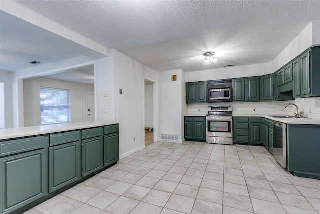 kitchen featuring appliances with stainless steel finishes, sink, green cabinets, light tile patterned floors, and kitchen peninsula