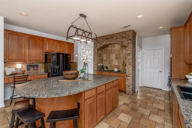 kitchen with black fridge, dark stone countertops, a kitchen island, pendant lighting, and backsplash