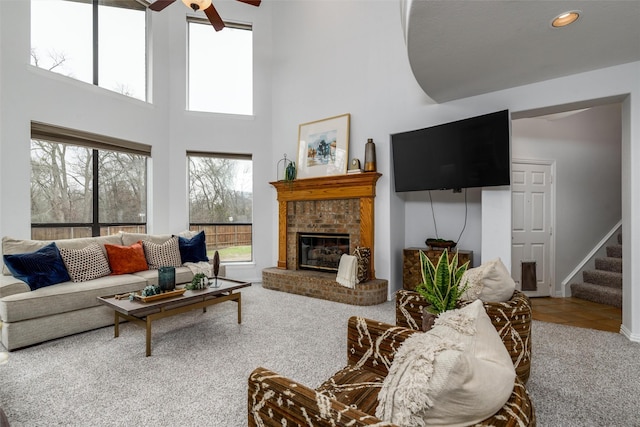 carpeted living room featuring a fireplace, ceiling fan, and a high ceiling