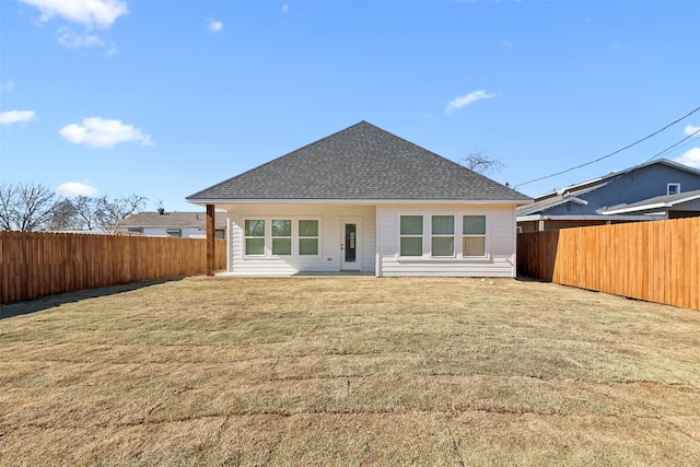 rear view of house with a yard, a shingled roof, and a fenced backyard