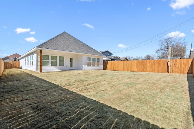 back of house featuring a shingled roof, a lawn, and a fenced backyard