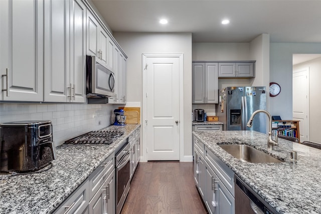 kitchen with gray cabinets, dark hardwood / wood-style floors, sink, stainless steel appliances, and light stone countertops