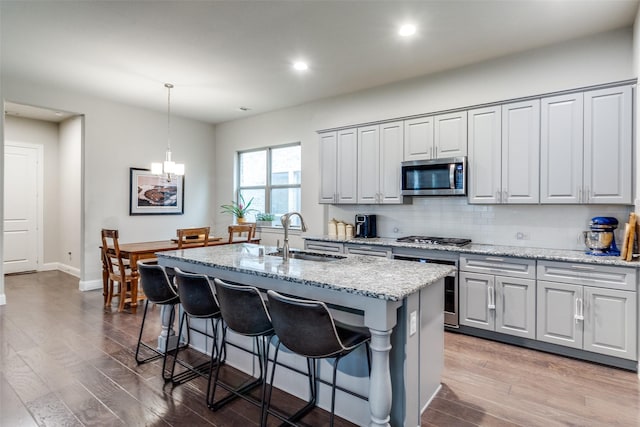 kitchen featuring appliances with stainless steel finishes, decorative light fixtures, sink, a kitchen island with sink, and light stone counters