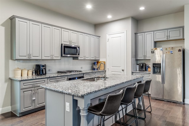 kitchen featuring sink, light stone counters, a center island with sink, appliances with stainless steel finishes, and dark hardwood / wood-style flooring