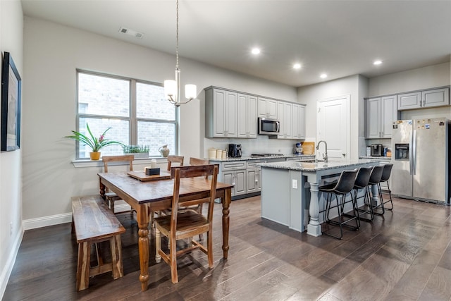 kitchen with gray cabinetry, a center island with sink, dark hardwood / wood-style floors, and appliances with stainless steel finishes