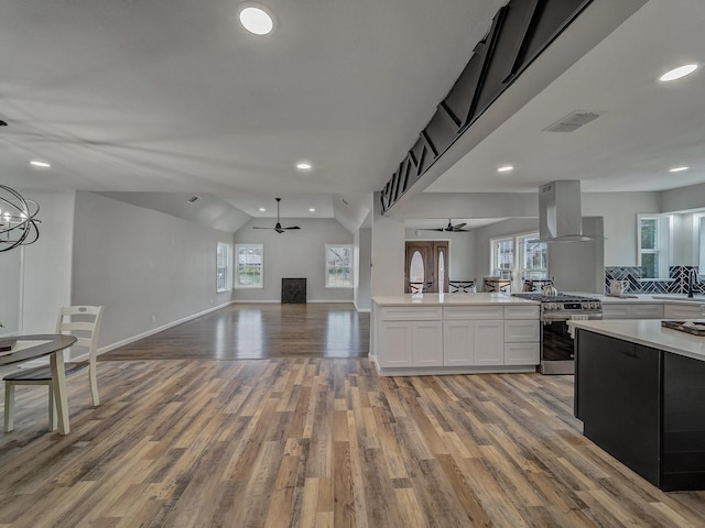 kitchen featuring light hardwood / wood-style flooring, island range hood, stainless steel gas range oven, white cabinets, and ceiling fan with notable chandelier