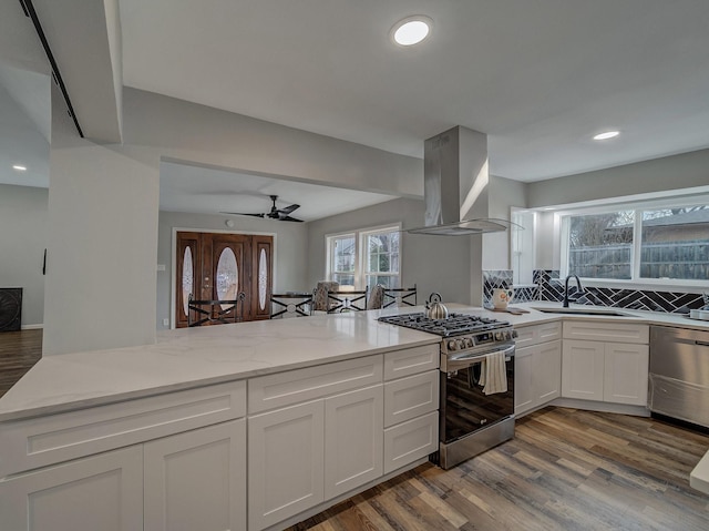 kitchen with appliances with stainless steel finishes, island range hood, sink, white cabinets, and light stone counters