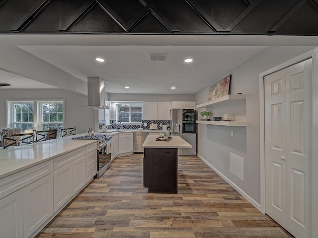 kitchen with island range hood, a center island, appliances with stainless steel finishes, light hardwood / wood-style floors, and white cabinets