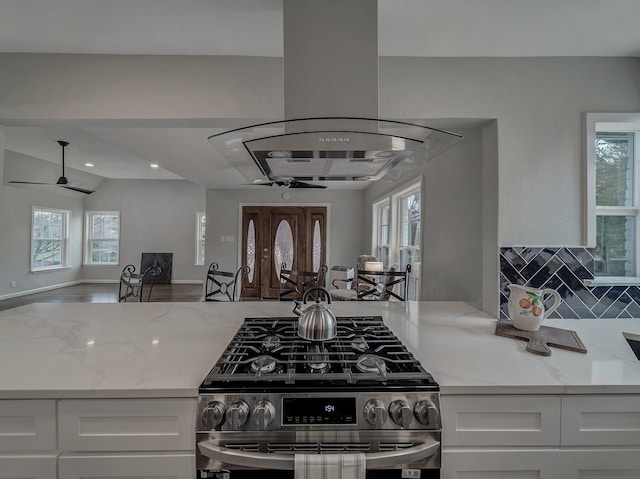 kitchen featuring stainless steel gas range oven, light stone countertops, white cabinets, and island exhaust hood