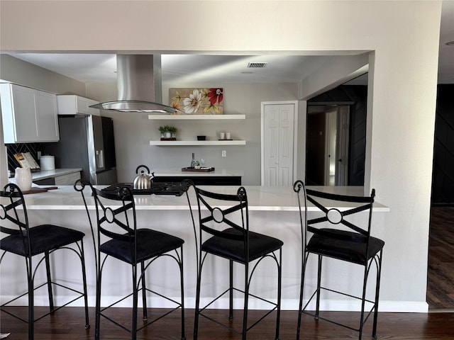 kitchen with island range hood, white cabinets, stainless steel fridge, backsplash, and kitchen peninsula