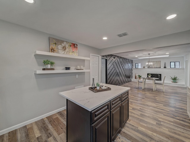 kitchen with light stone counters, decorative light fixtures, dark brown cabinets, light hardwood / wood-style flooring, and a kitchen island