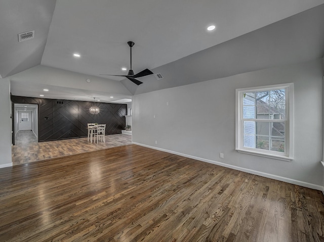 unfurnished living room with ceiling fan, vaulted ceiling, wooden walls, and wood-type flooring