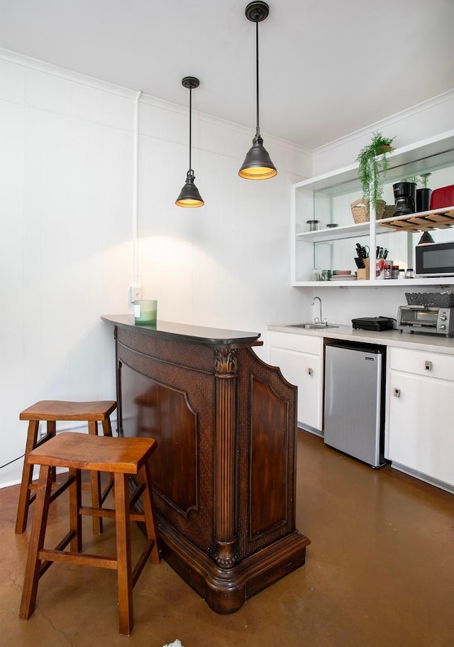 bar featuring dishwashing machine, sink, stainless steel refrigerator, white cabinetry, and hanging light fixtures