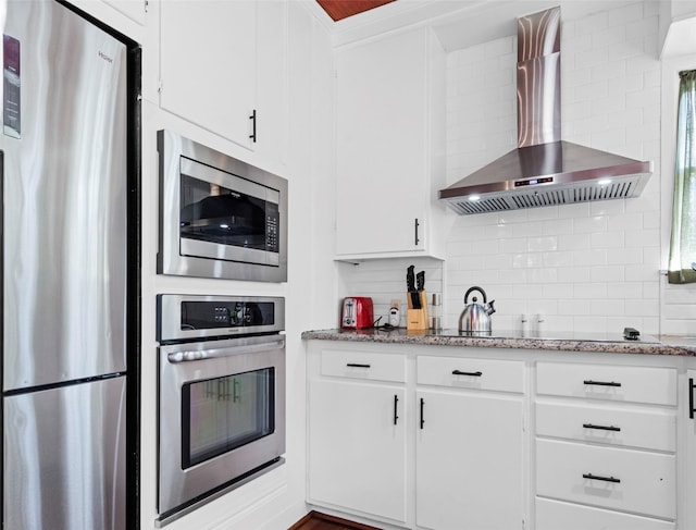 kitchen featuring white cabinetry, appliances with stainless steel finishes, light stone countertops, and wall chimney range hood