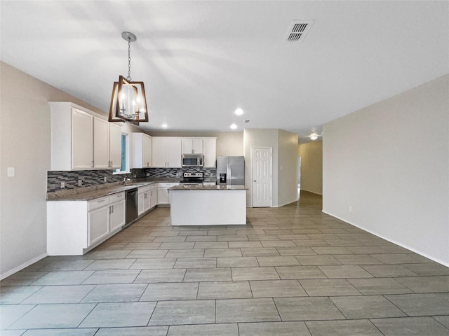 kitchen featuring tasteful backsplash, decorative light fixtures, a center island, appliances with stainless steel finishes, and white cabinets