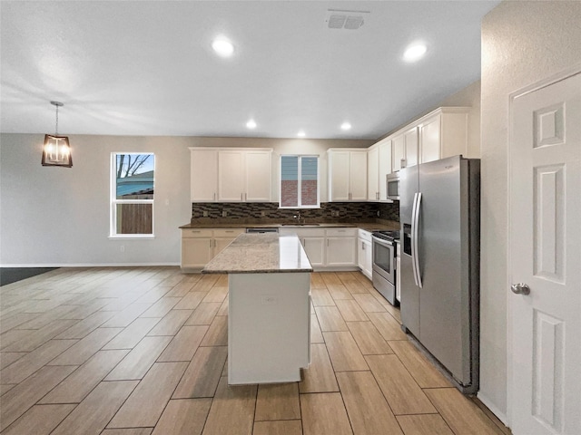 kitchen featuring tasteful backsplash, white cabinets, hanging light fixtures, a center island, and stainless steel appliances